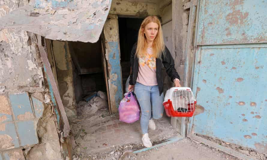 A woman carries her belongings and a cat while leaving a damaged house following recent shelling in the Petrovsky district of Donetsk