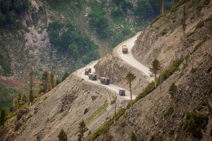 Army trucks drive along a track winding up a mountainside