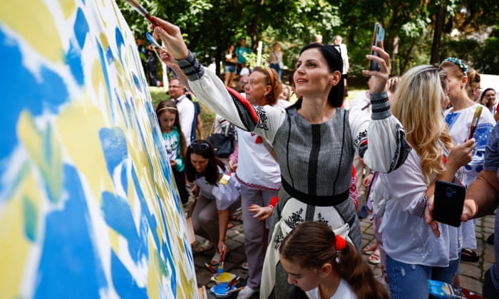 People paint a white canvas the blue and yellow colours of the Ukrainian flag during a ceremony in the Na Valakh park on the Independence Day of Ukraine.