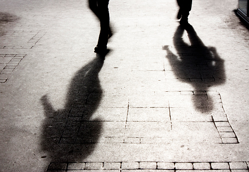 Shadow of a man on patterened sidewalk following the shadow of another person